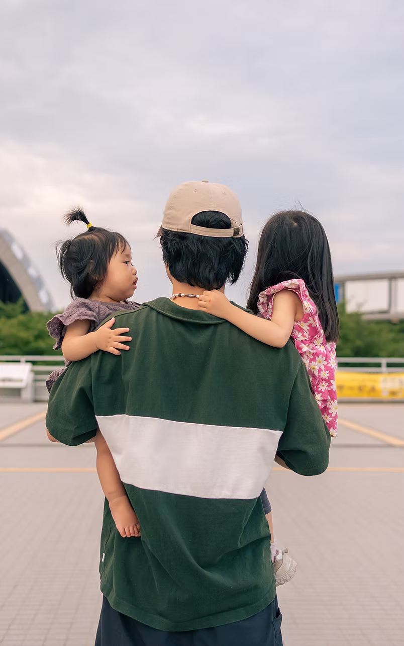 子どもふたりを抱えて歩く父親の後ろ姿
